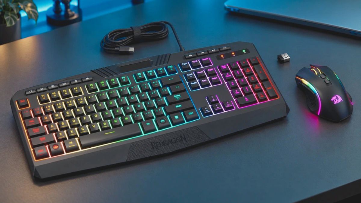 Black RGB gaming keyboard and mouse on a dark desk beside a USB cable and wireless receiver.